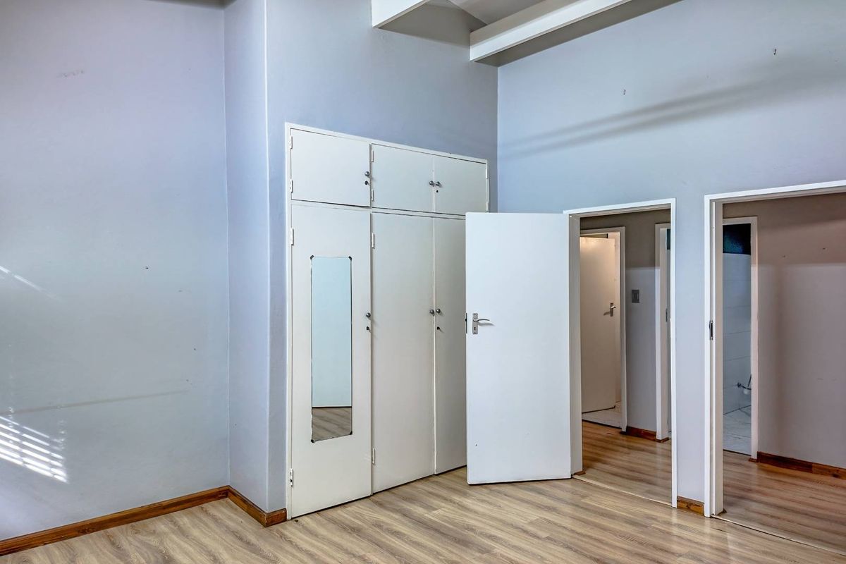 A bedroom featuring built-in floor-to-ceiling wardrobes with integrated mirror and laminate wood flooring, providing access to adjacent rooms.