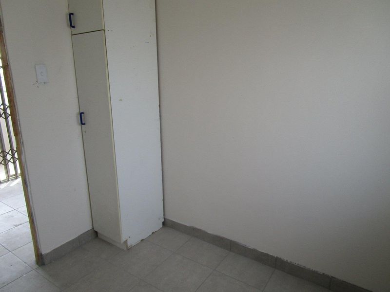 An empty bedroom featuring tiled flooring, a built-in cupboard, and access to an exterior area through a security gate.