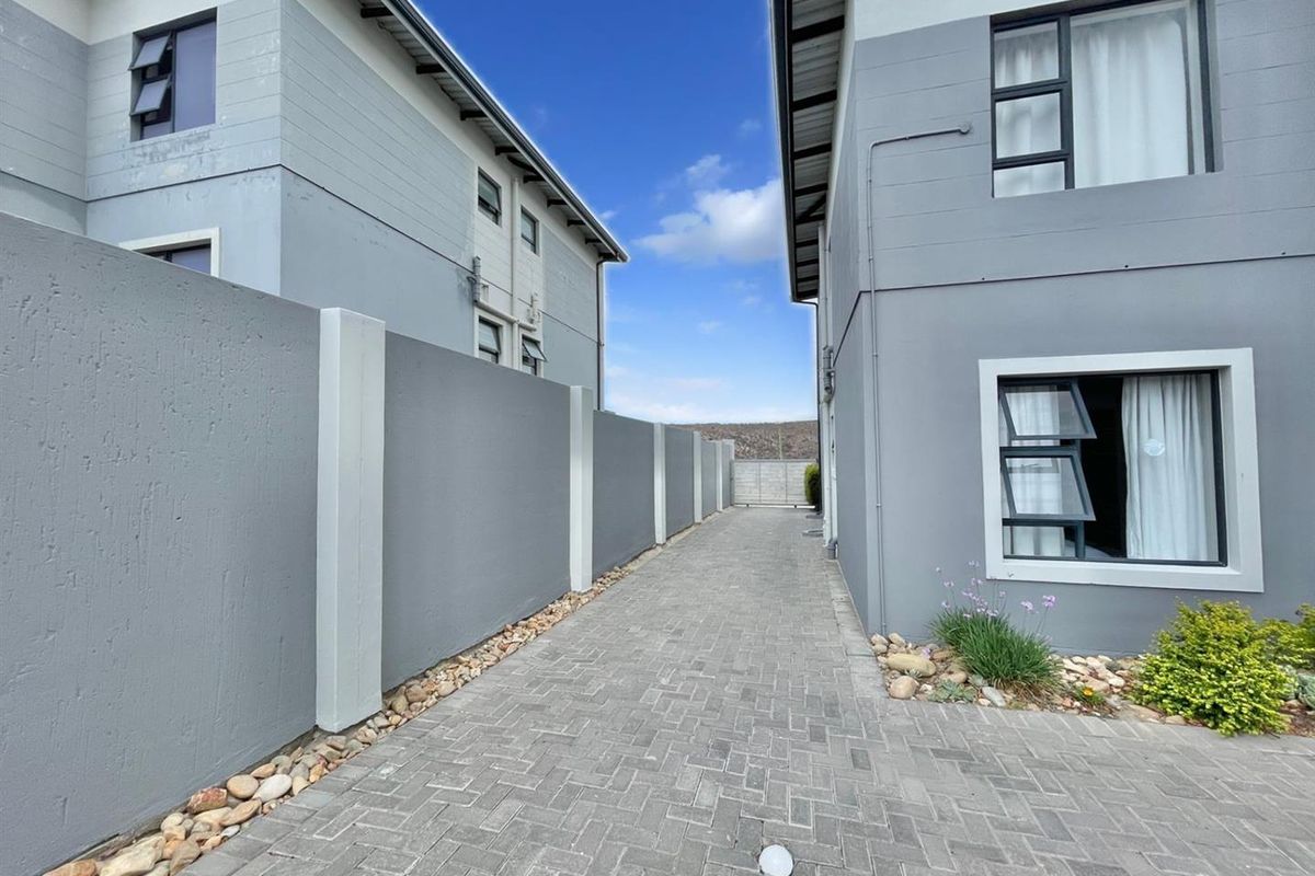 A clean, paved side passage between two modern residential buildings, featuring grey rendered boundary walls and neat pebble landscaping.