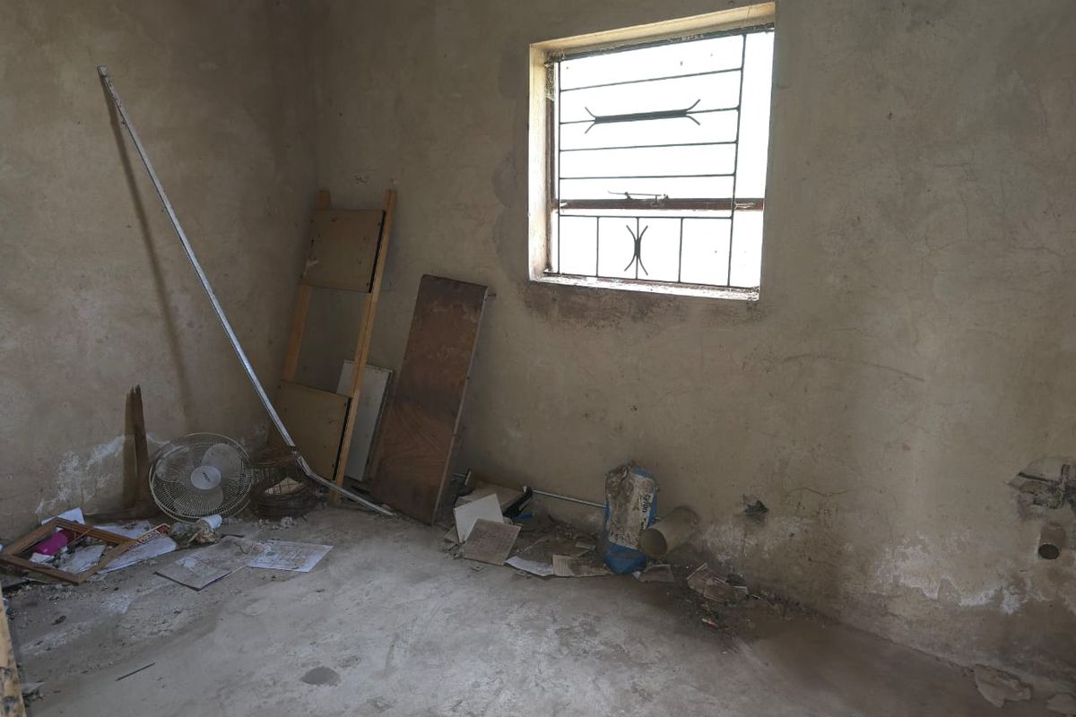 An unfinished bedroom space featuring concrete flooring and a window with security bars, requiring significant renovation and cosmetic updates.
