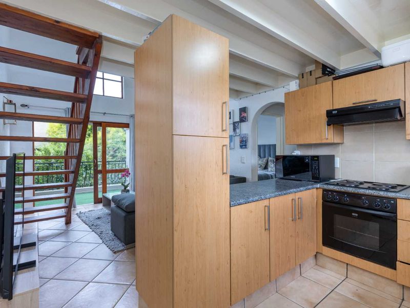 Open-plan kitchen featuring light wood cabinetry, granite countertops, and integrated appliances, adjacent to a wooden staircase leading to an upper level.