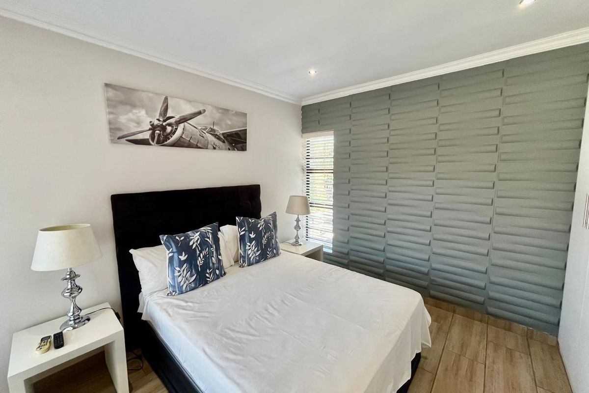 A well-maintained bedroom featuring wood-look tile flooring, a modern textured feature wall, recessed downlighting, and crown molding.
