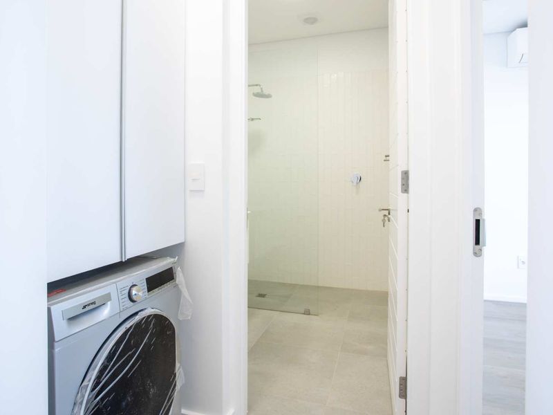 A clean, modern laundry area featuring built-in cabinetry and direct access to a contemporary walk-in shower with tiled finishes.