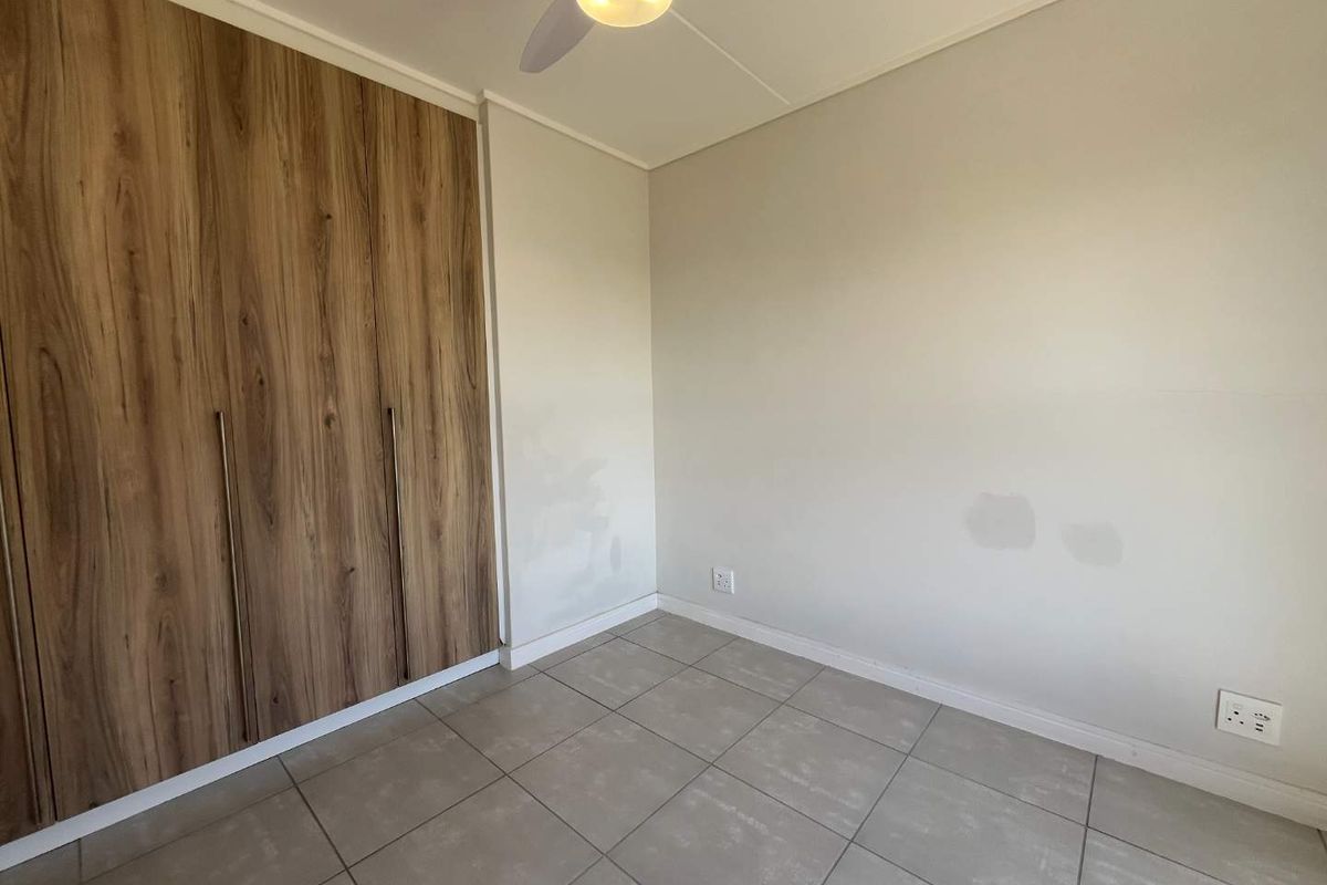 A clean, empty bedroom featuring modern wood-finish built-in cupboards, neutral tiled flooring, and a ceiling fan, ready for personalization.