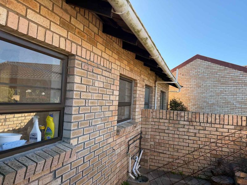 Rear exterior view of the townhouse featuring face brick construction, aluminium window frames, and existing guttering system.
