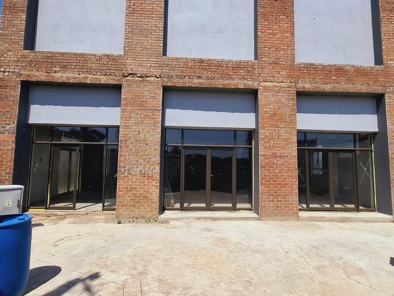 Front elevation of a commercial building featuring exposed brickwork, large aluminium-framed glass entrance doors, and a concrete forecourt area.