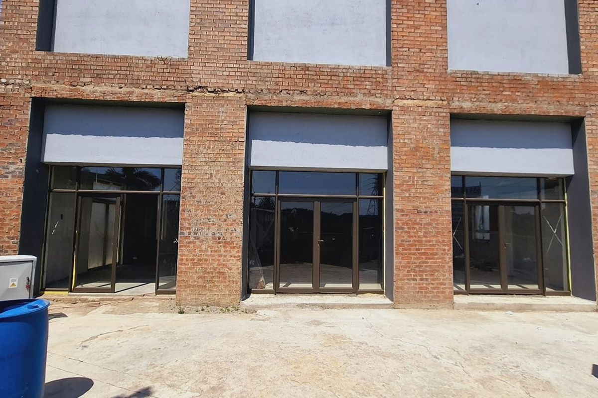 Front elevation of a commercial building featuring exposed brickwork, large aluminium-framed glass entrance doors, and a concrete forecourt area.