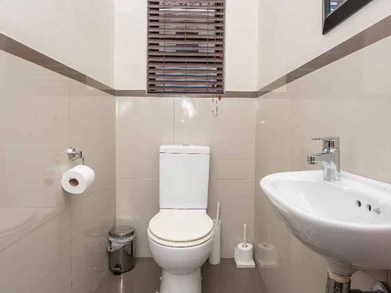 A compact, well-maintained guest bathroom featuring neutral wall tiles, a modern wall-mounted basin with chrome fixtures, and a standard toilet.