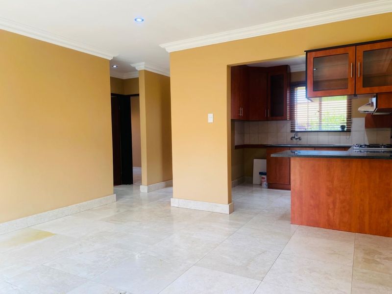 Open plan living area featuring tiled floors and a semi-enclosed kitchen with built-in wooden cabinetry and granite countertops.