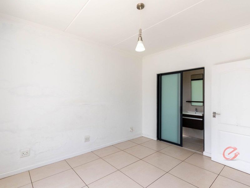 An empty bedroom featuring tiled flooring, a modern pendant light, and a sliding door providing access to an en-suite bathroom.