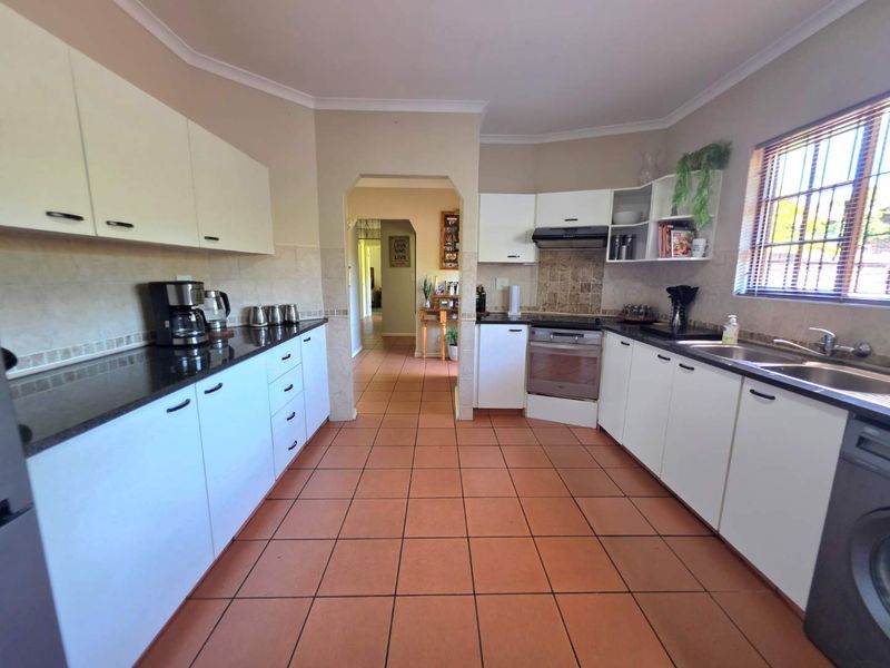 Functional kitchen featuring white cabinetry, dark granite countertops, tiled backsplash, built-in oven, extractor fan, and tiled flooring with a view into the hallway.