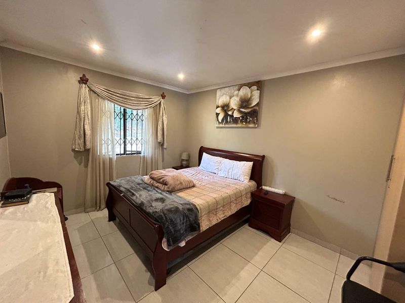 A functional bedroom featuring tiled flooring, recessed downlighting, and a secure window with a fitted security gate.
