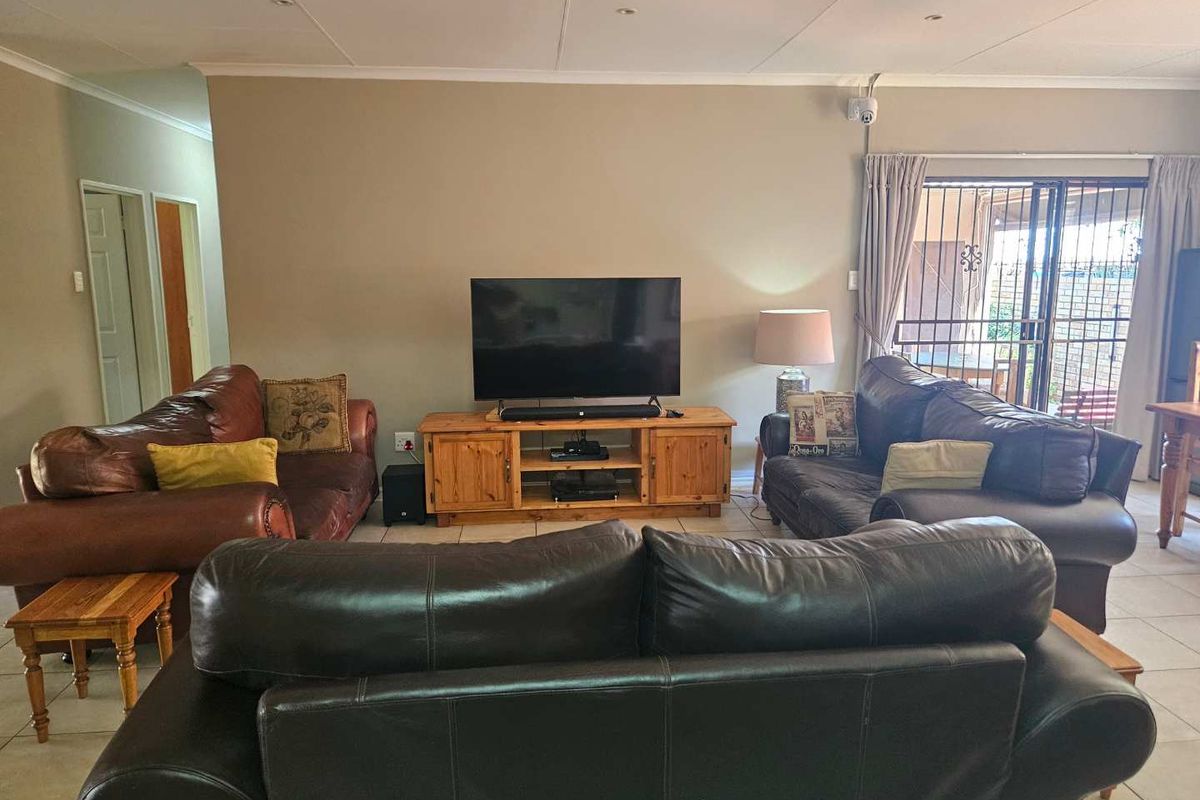 A spacious living room featuring tiled flooring, recessed ceiling lighting, and sliding glass doors with security gates leading to an outdoor area.