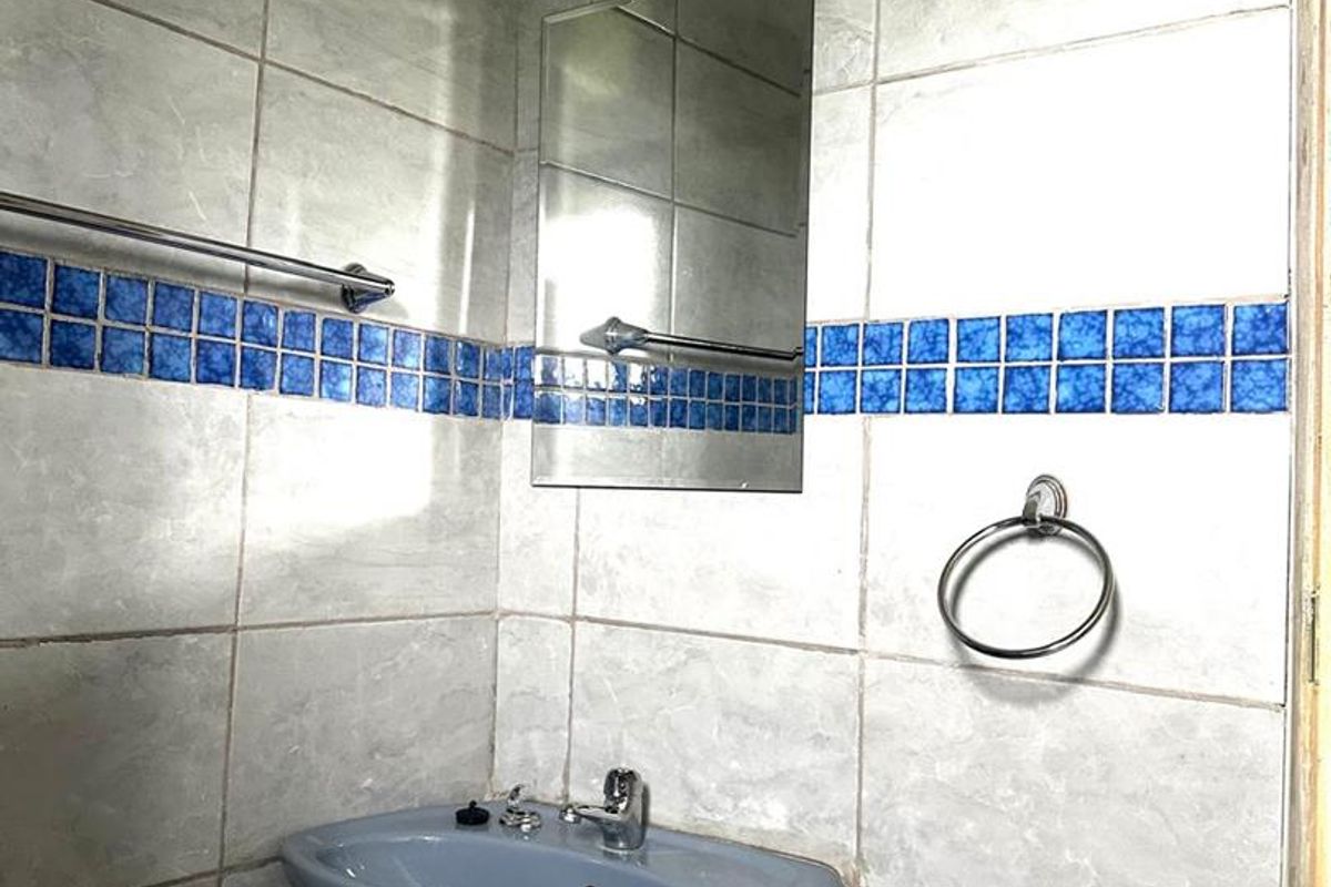 A compact bathroom featuring a pedestal basin, wall-mounted mirror, and decorative blue accent tiling.