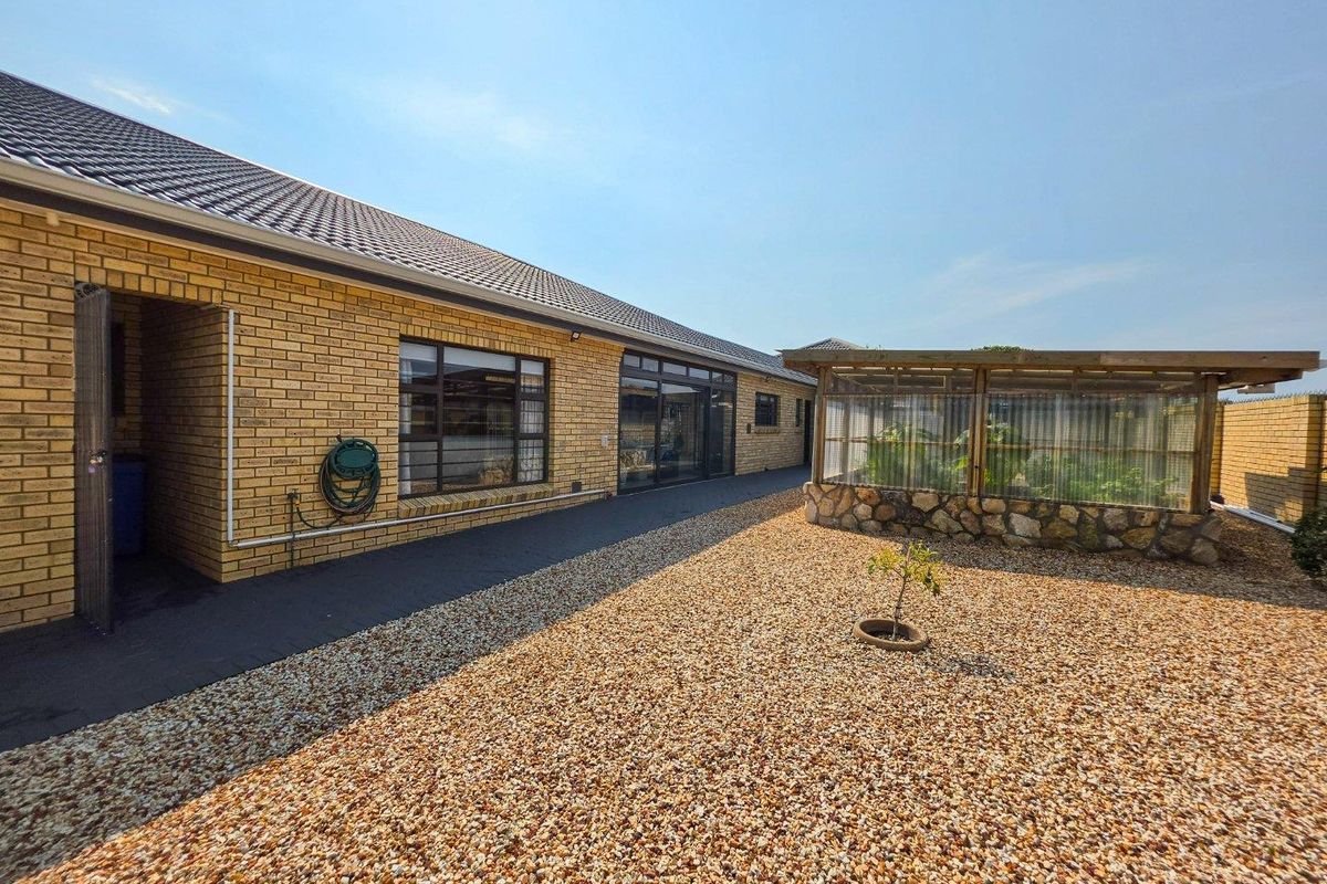 Rear exterior view of the property featuring a brick facade, gravel landscaping, and a small greenhouse structure.