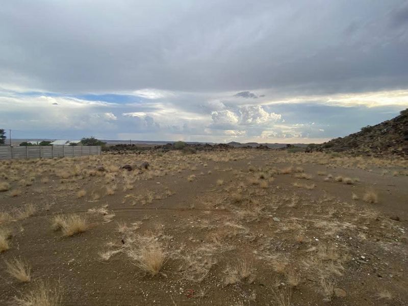 A wide-angle view of a vacant residential plot featuring natural arid landscape and a precast concrete boundary wall.