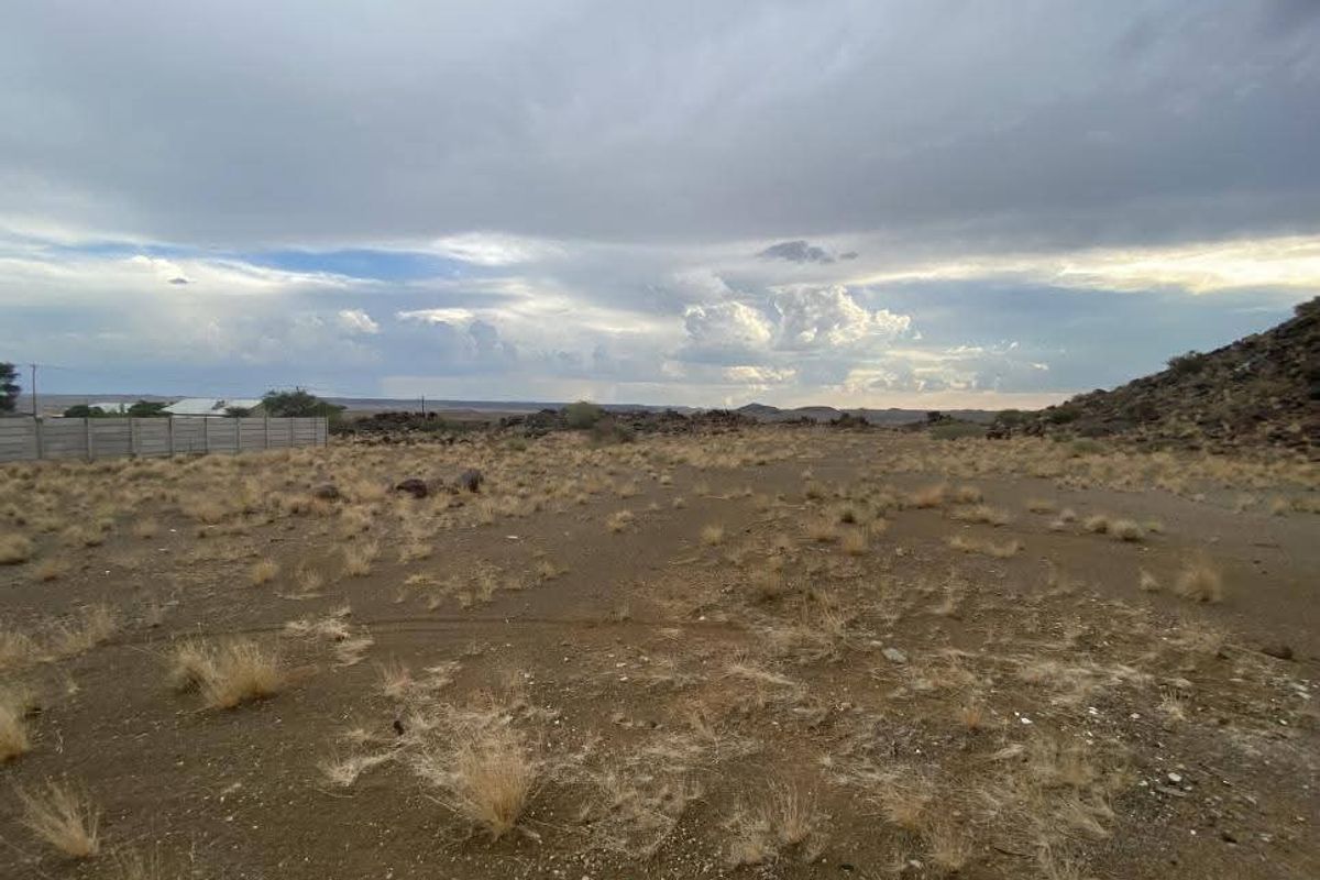 A wide-angle view of a vacant residential plot featuring natural arid landscape and a precast concrete boundary wall.