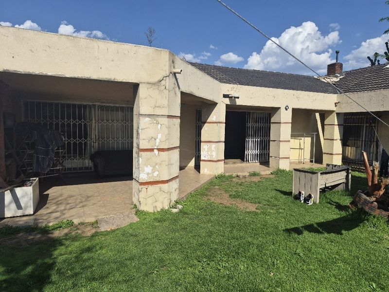 Rear view of the property featuring a covered patio area with security gates and a garden space, showing signs of exterior wear.