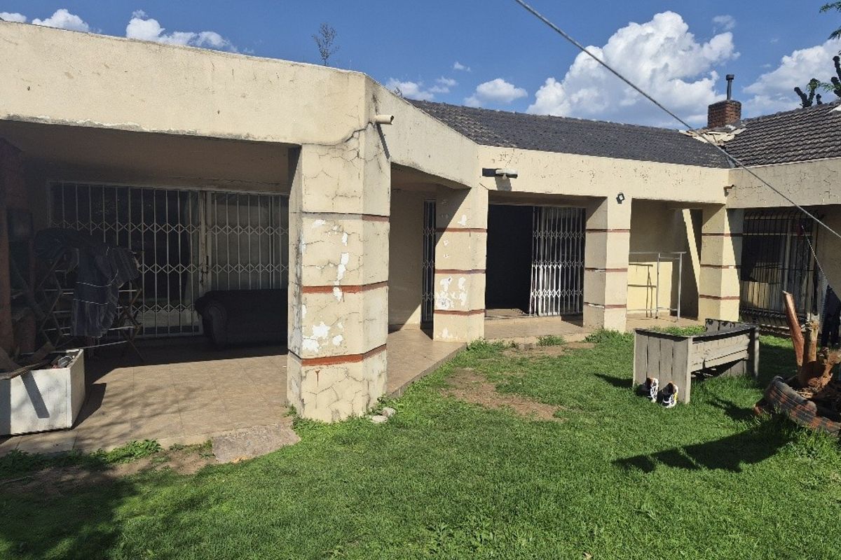 Rear view of the property featuring a covered patio area with security gates and a garden space, showing signs of exterior wear.