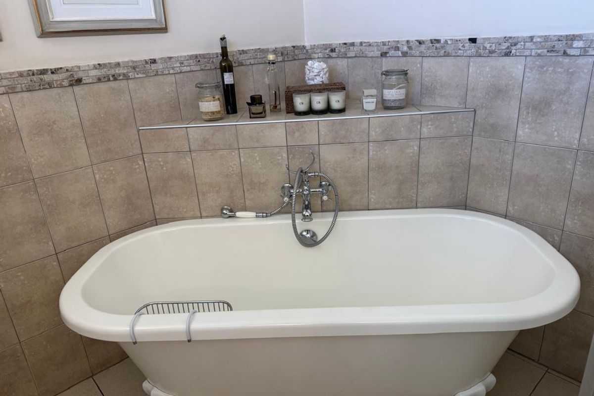 A classic clawfoot bathtub featuring a chrome telephone-style faucet and handheld shower attachment, set against neutral tiled walls with a decorative mosaic border.
