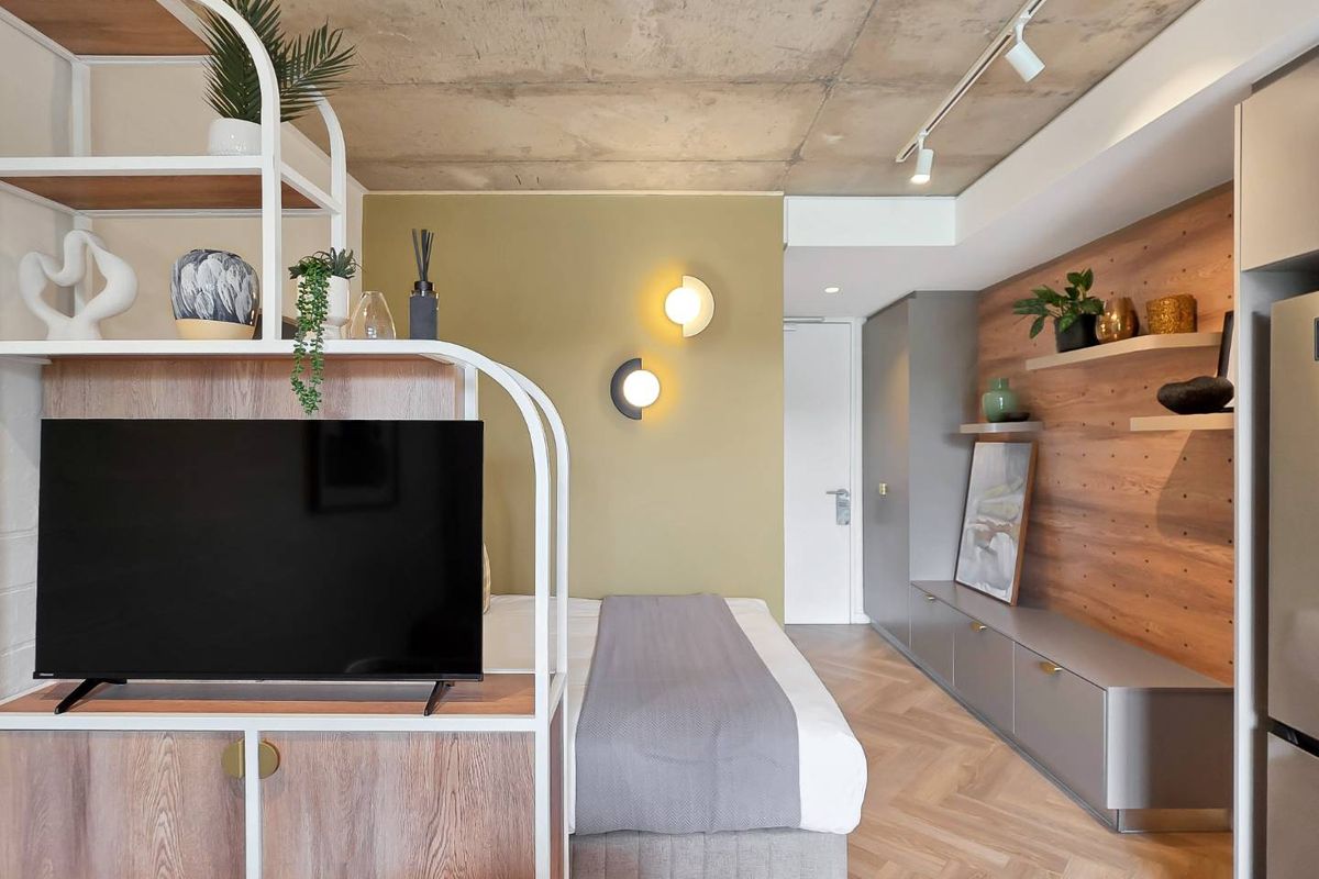 Modern studio bedroom featuring exposed concrete ceilings, herringbone flooring, custom built-in cabinetry, and stylish timber wall paneling with integrated lighting.