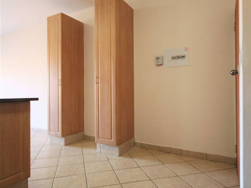 A clean, empty kitchen area featuring light wood-toned built-in cabinetry and neutral ceramic floor tiles.