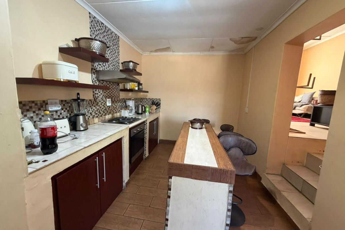 A dated kitchen featuring built-in cabinetry, a breakfast bar, and tiled surfaces, showing visible signs of ceiling water damage requiring repair.