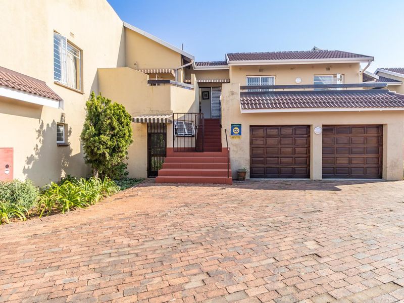 Front elevation of a townhouse featuring a double garage, brick paved driveway, and an elevated entrance staircase with security gates.