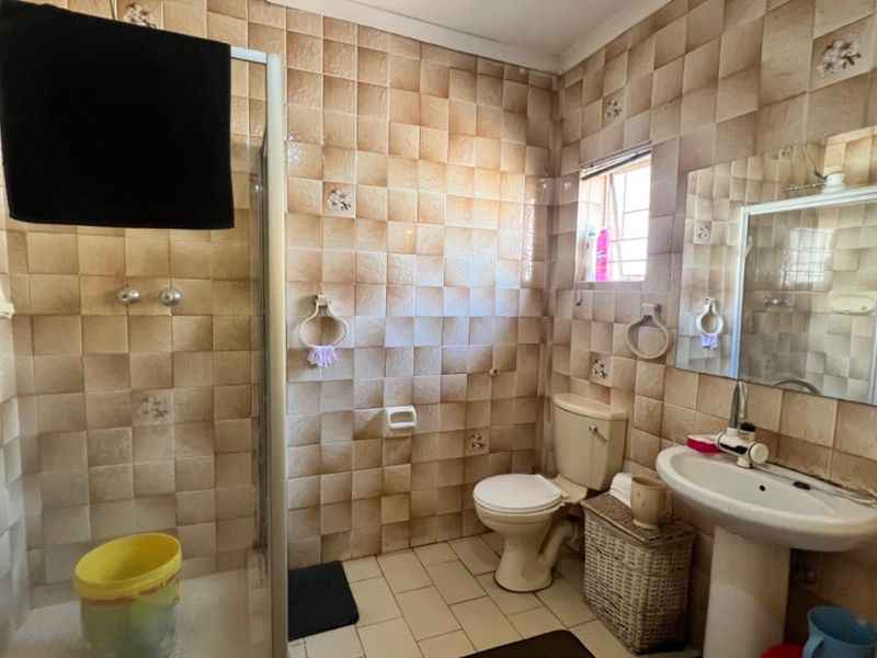 A functional bathroom featuring a shower enclosure, pedestal basin, and toilet, finished with dated wall tiling throughout.