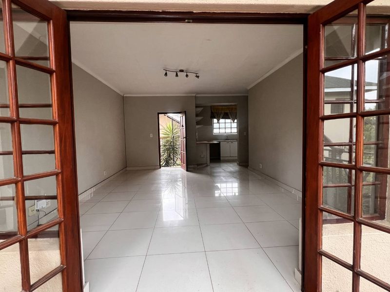 An open-plan living area featuring tiled flooring, track lighting, and direct access to a kitchen space through a bright, neutral interior.