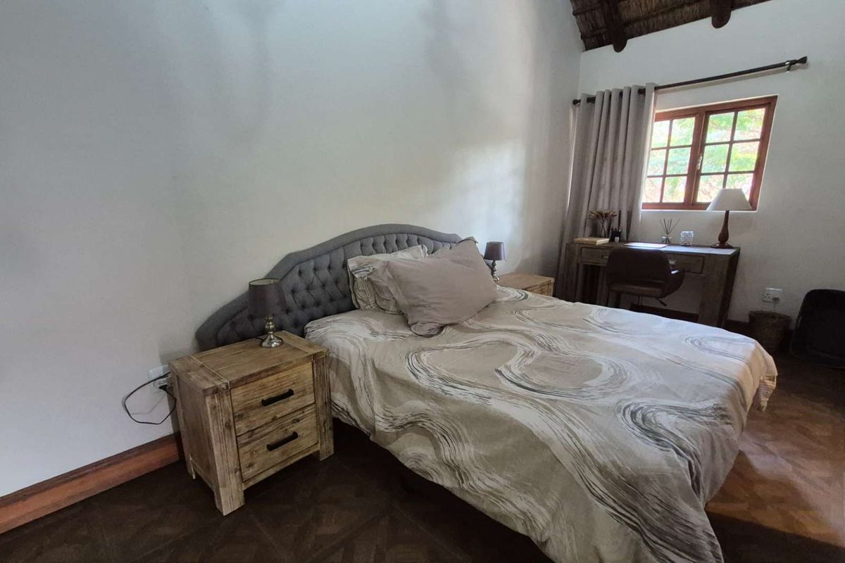 A cozy bedroom featuring exposed timber rafters, tiled flooring, and a window with natural light, offering a comfortable and rustic living space.