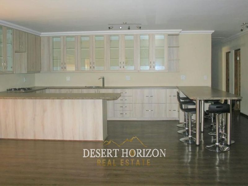 Spacious open-plan kitchen featuring light wood-finish cabinetry, laminate countertops, a breakfast bar, and dark laminate flooring.