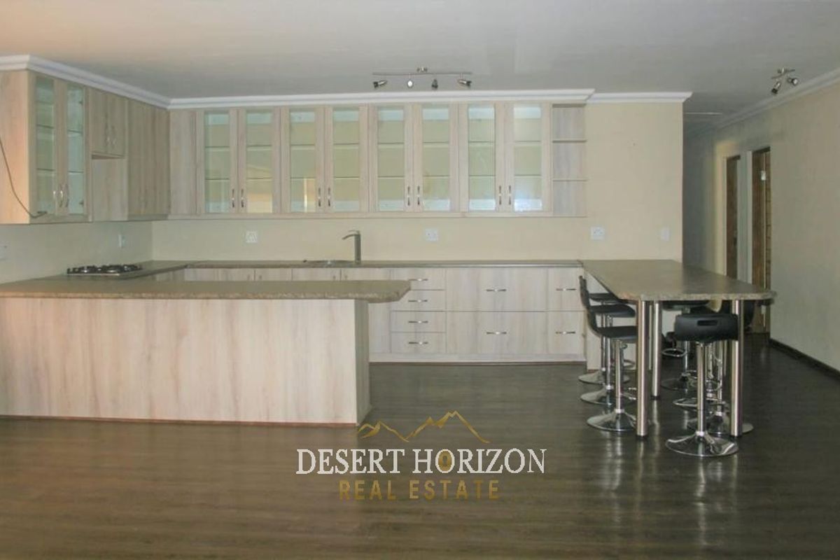 Spacious open-plan kitchen featuring light wood-finish cabinetry, laminate countertops, a breakfast bar, and dark laminate flooring.