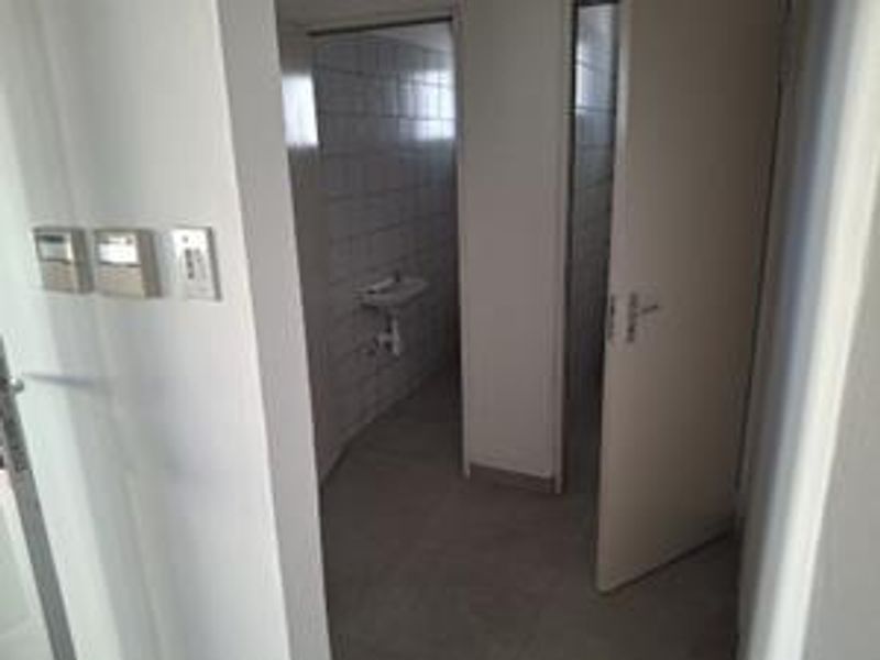 A functional office bathroom area featuring tiled walls, flooring, and a wall-mounted basin, presented in a clean, vacant state.