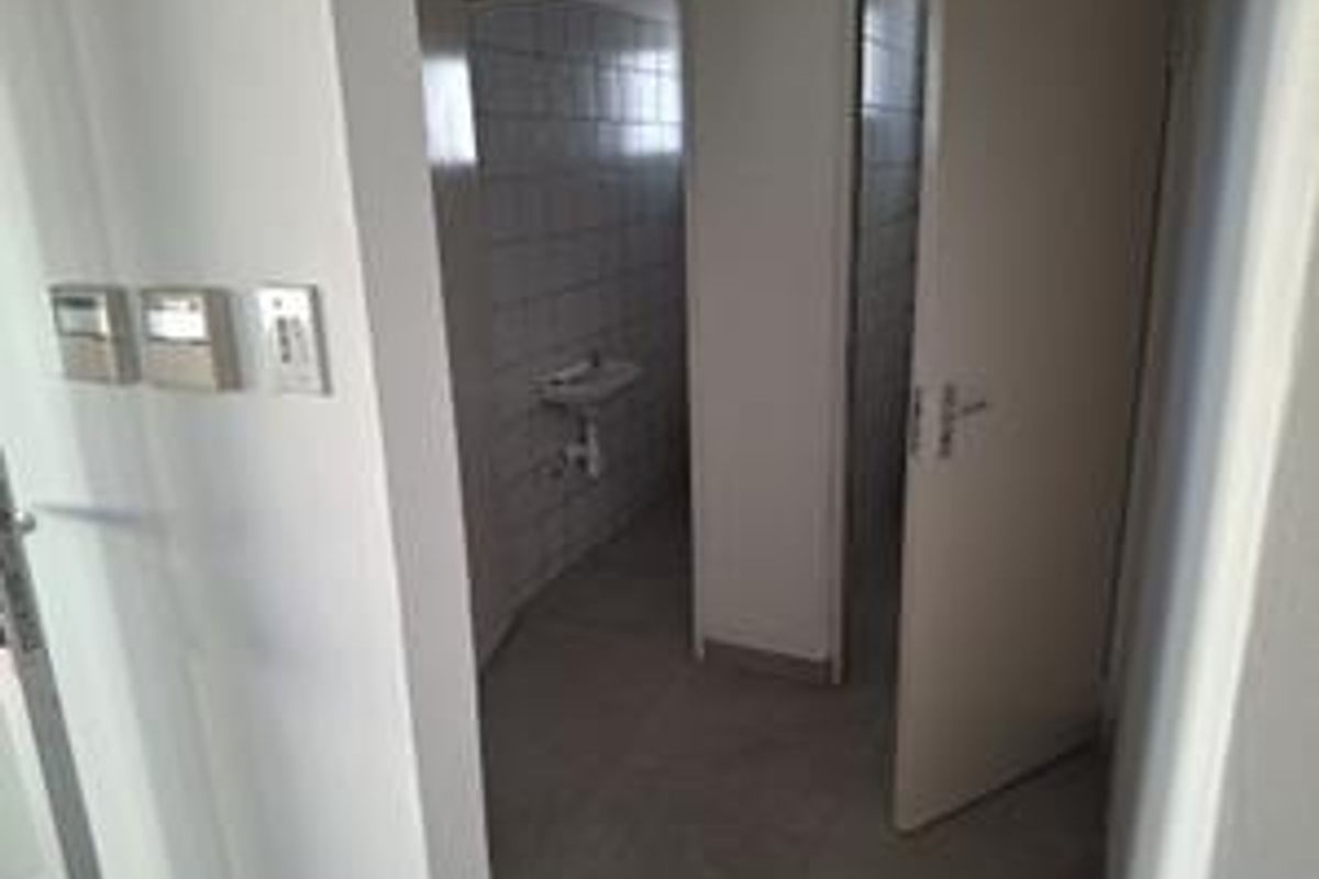 A functional office bathroom area featuring tiled walls, flooring, and a wall-mounted basin, presented in a clean, vacant state.