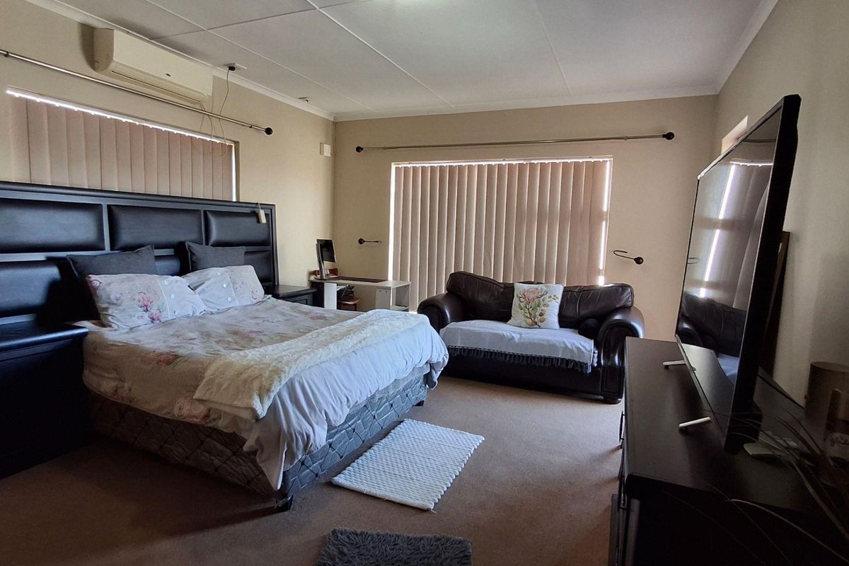 Spacious bedroom featuring carpet flooring, vertical blinds, and a wall-mounted split-system air conditioner.