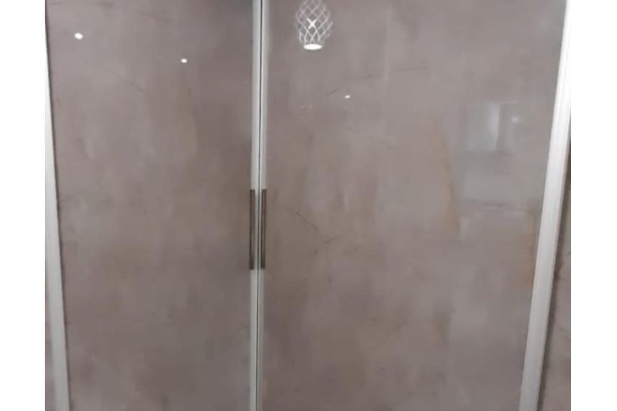 A corner view of a bedroom featuring modern built-in sliding door wardrobes with a smooth, neutral finish.