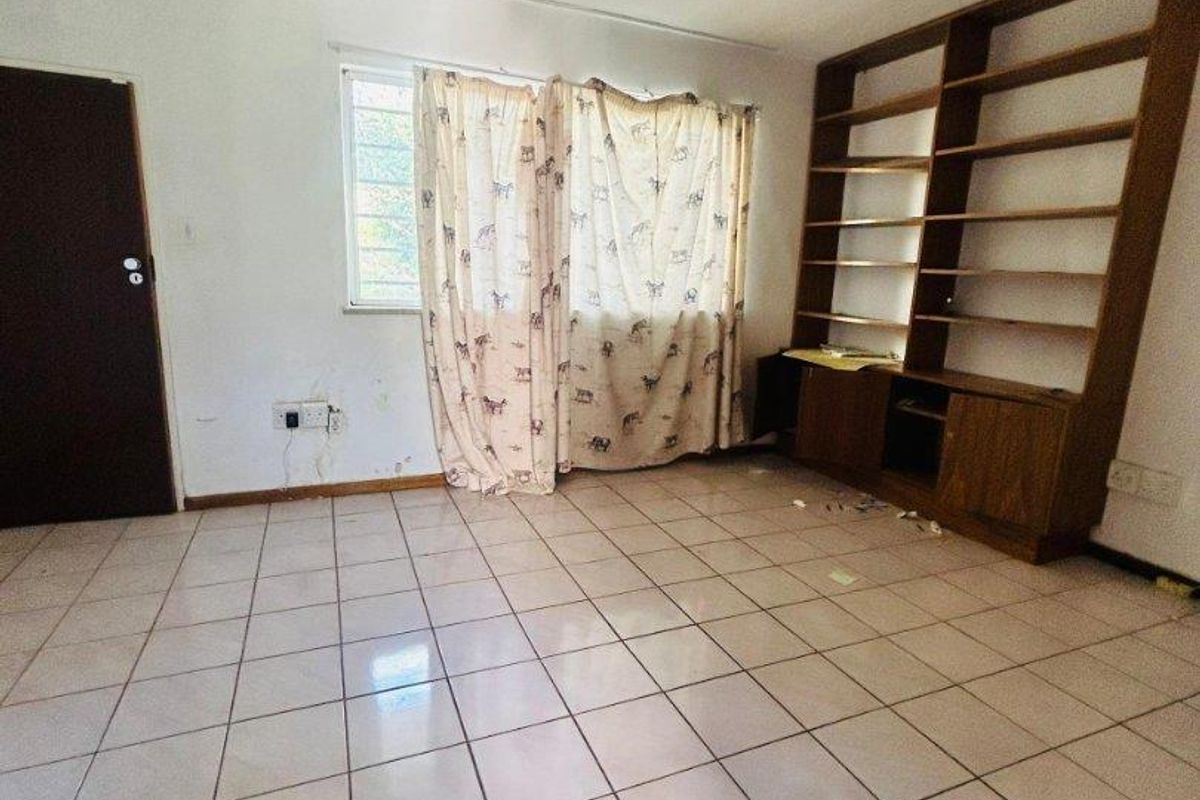 A vacant living room featuring tiled flooring, a ceiling fan, and built-in wooden shelving units, offering a blank canvas for potential updates.