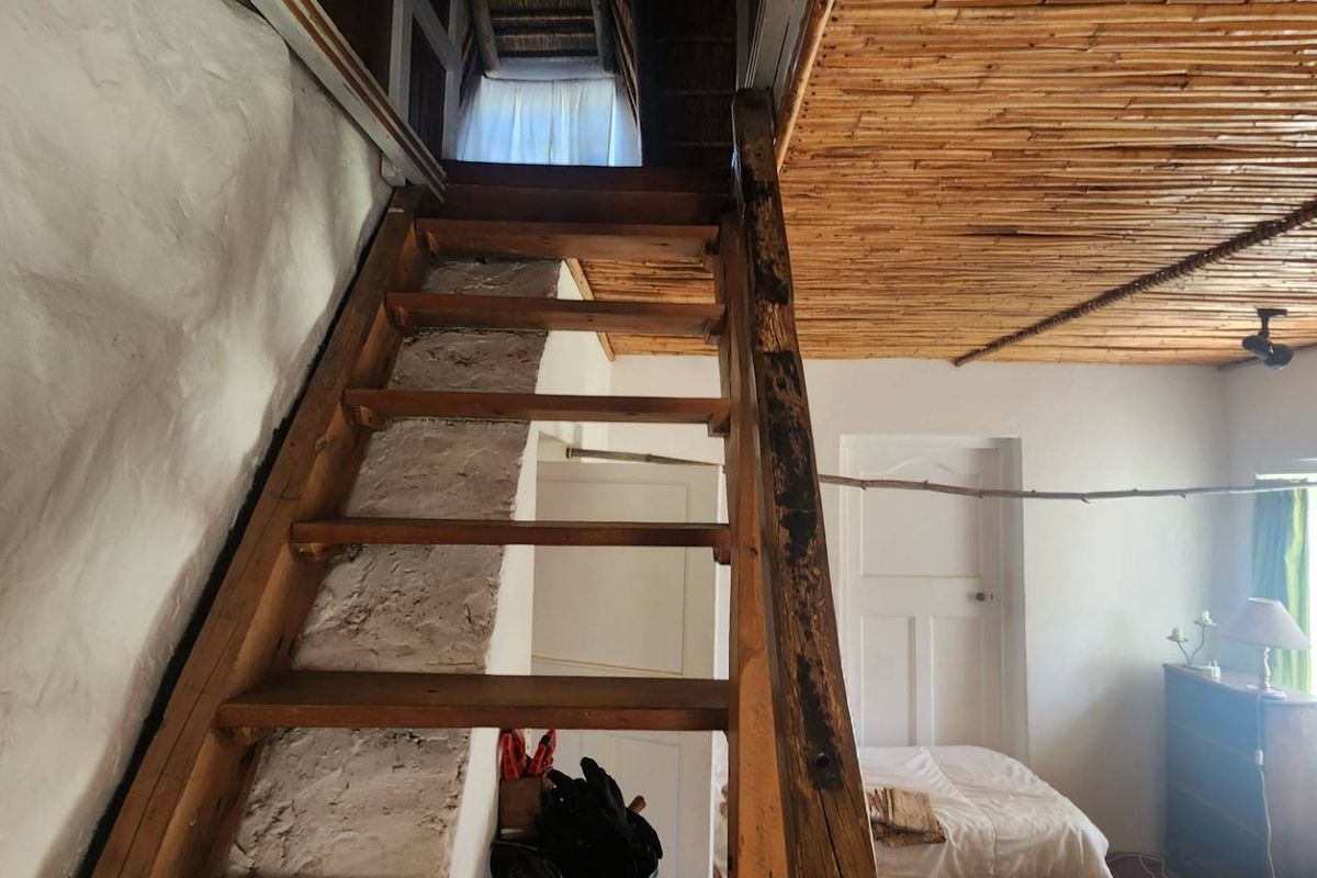 A rustic interior space featuring a wooden staircase leading to an upper level, with a traditional reed ceiling and white plastered walls.