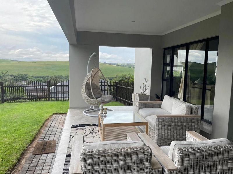 A covered patio area featuring tiled flooring and sliding glass doors, offering scenic views of the surrounding landscape and garden.