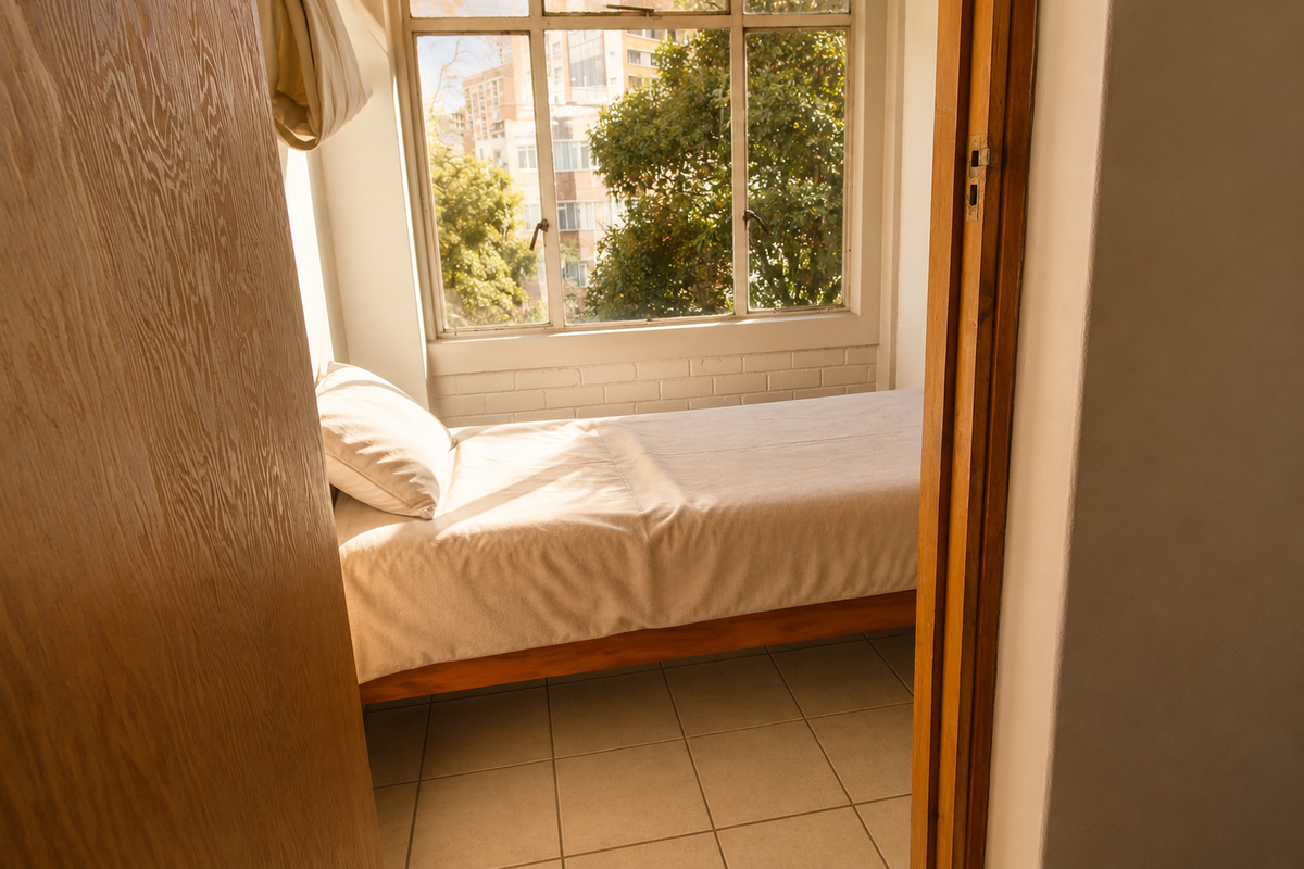 A compact bedroom featuring tiled flooring, a large window providing natural light, and painted brick wall detailing.