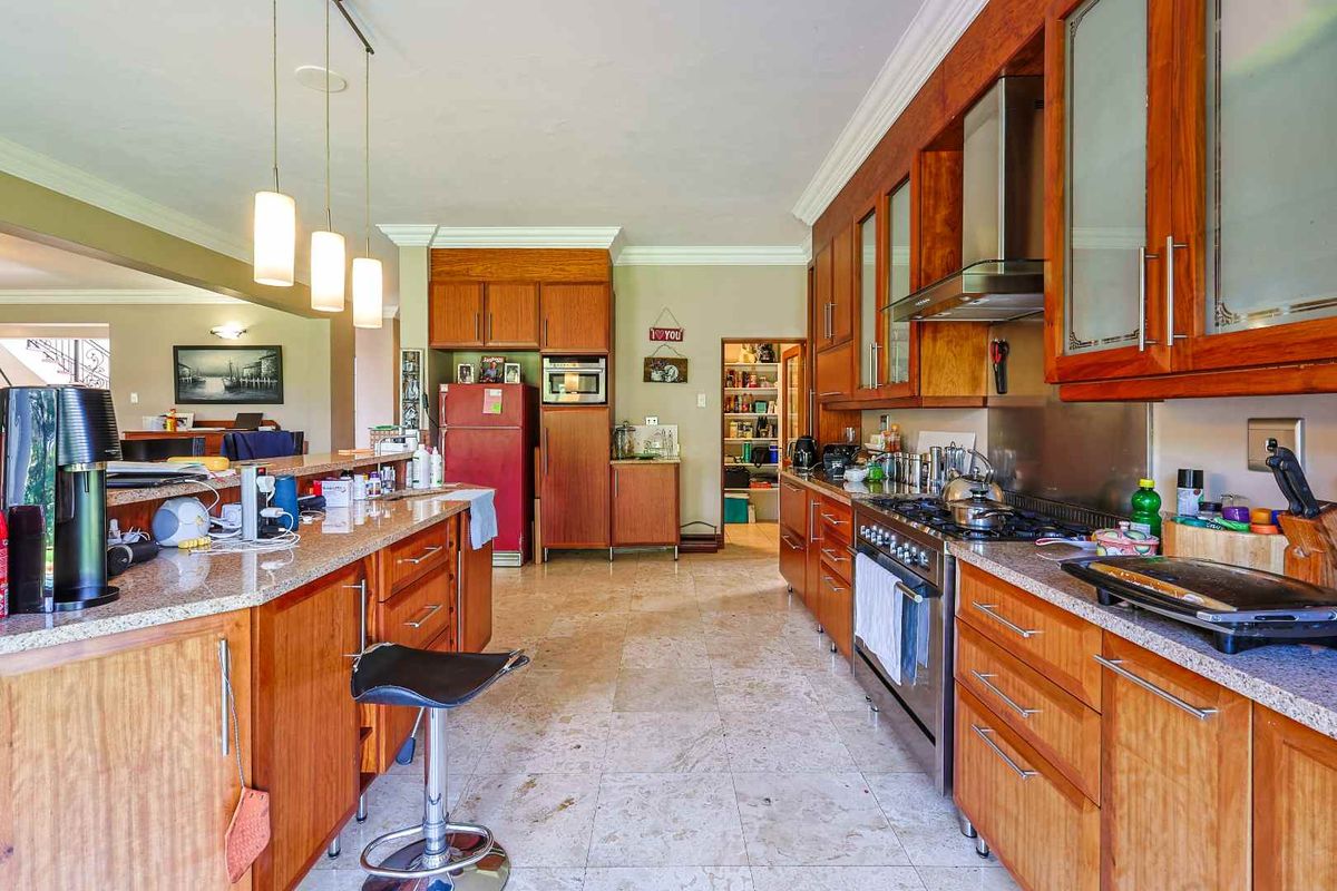 Spacious kitchen featuring warm wooden cabinetry, granite countertops, stainless steel appliances, and a convenient walk-in pantry, flowing into an open-plan living area.