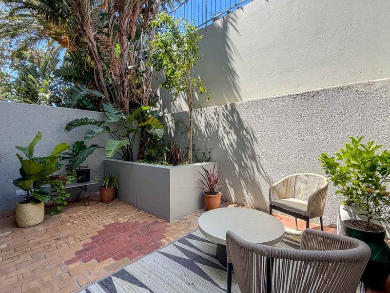 A private outdoor patio area featuring brick paving, a built-in raised planter box, and high boundary walls for added privacy.