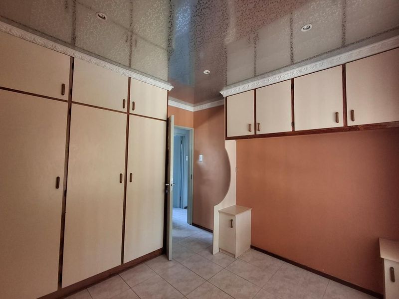 A bedroom featuring extensive built-in cabinetry, tiled flooring, and a unique reflective ceiling finish, offering a functional space ready for personalization.
