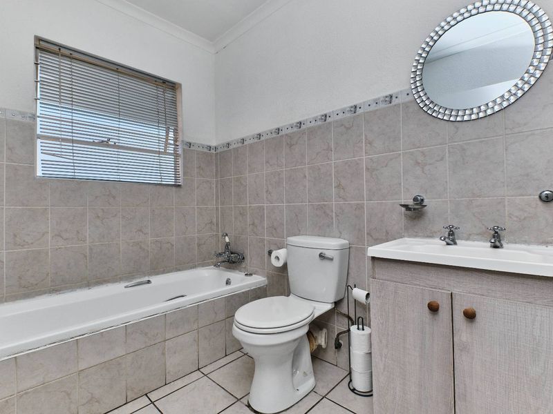 A functional bathroom featuring a bathtub, toilet, and vanity basin with neutral wall and floor tiling.