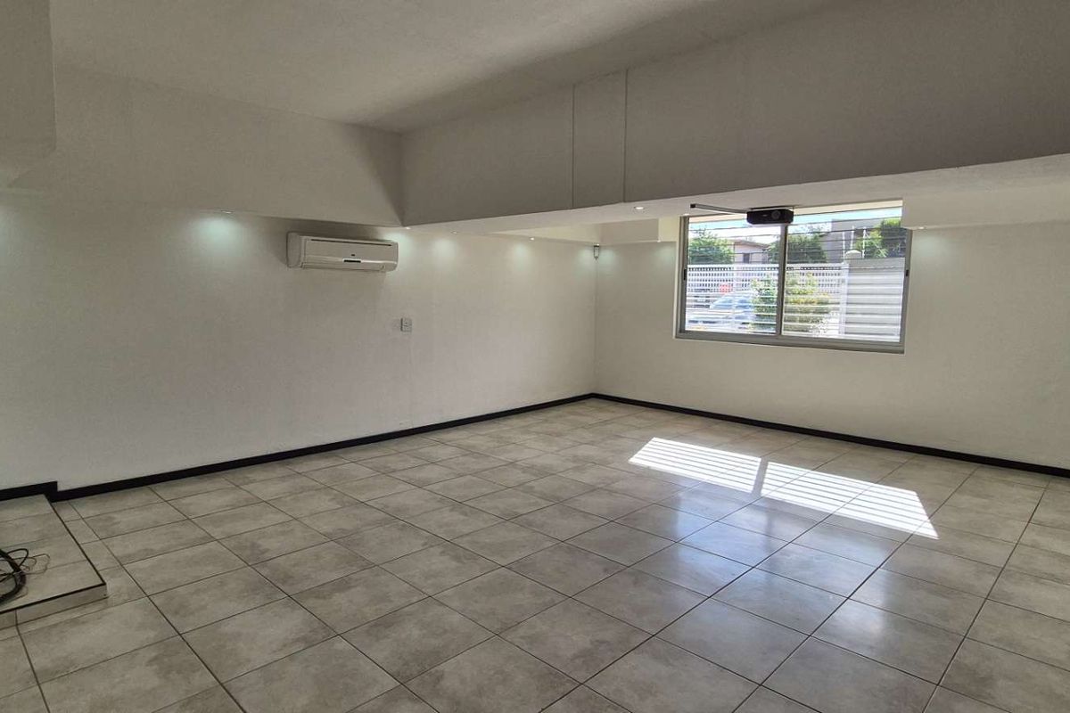 A spacious, open-plan living area featuring neutral floor tiles, recessed ceiling lighting, a wall-mounted air conditioning unit, and a built-in fireplace.