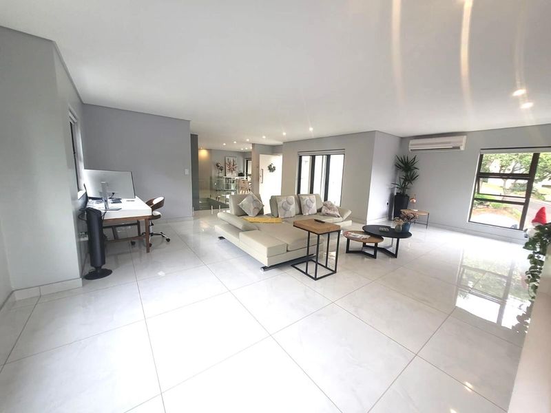 Spacious open-plan living area featuring large format floor tiles, recessed lighting, and a wall-mounted air conditioning unit with neutral wall finishes.