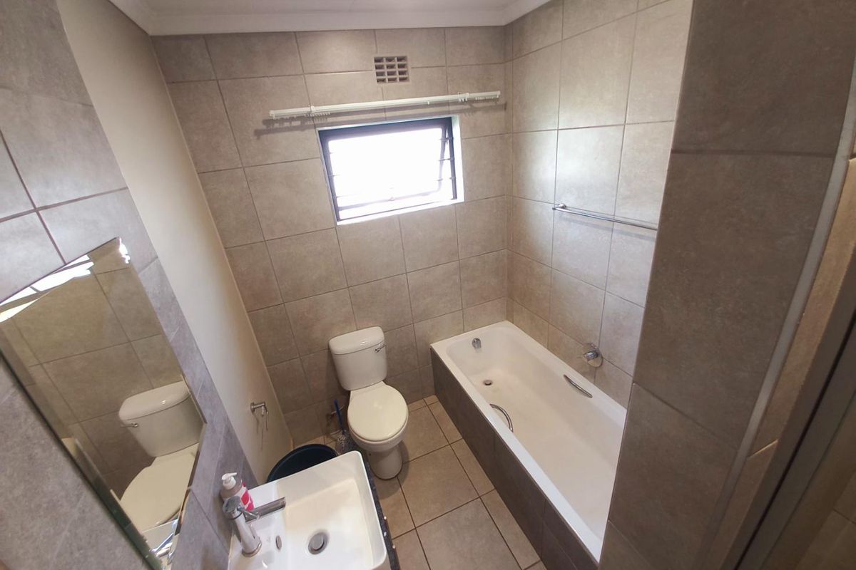 A functional bathroom featuring neutral wall and floor tiling, a built-in bathtub, a standard toilet, and a wall-mounted basin.
