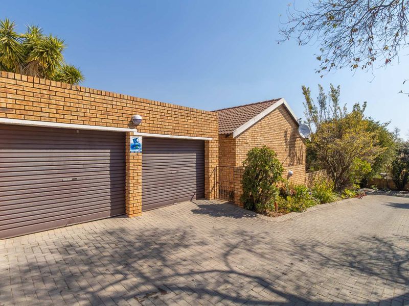 Front view of a townhouse featuring a double garage with roller doors, brick exterior, and a paved driveway.