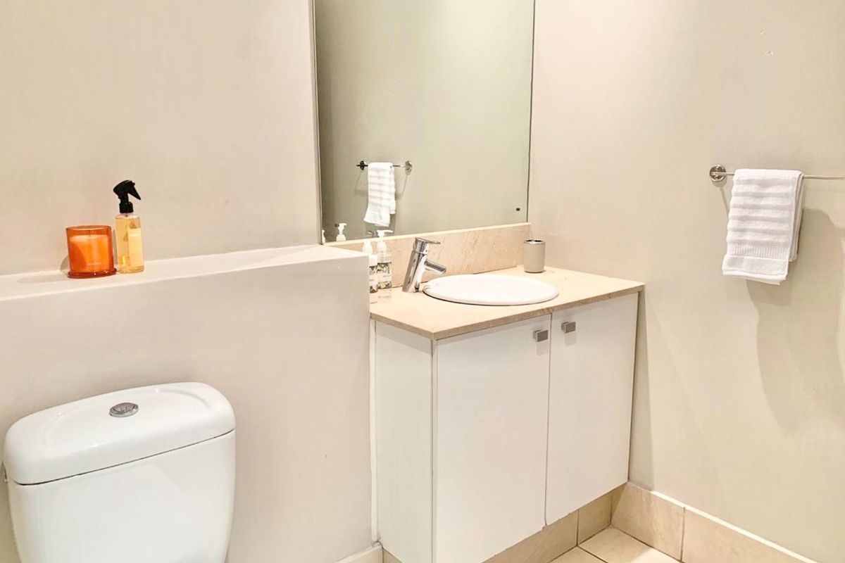 A clean and functional bathroom featuring a vanity cabinet with stone countertop, integrated basin, wall-mounted mirror, and a modern dual-flush toilet.